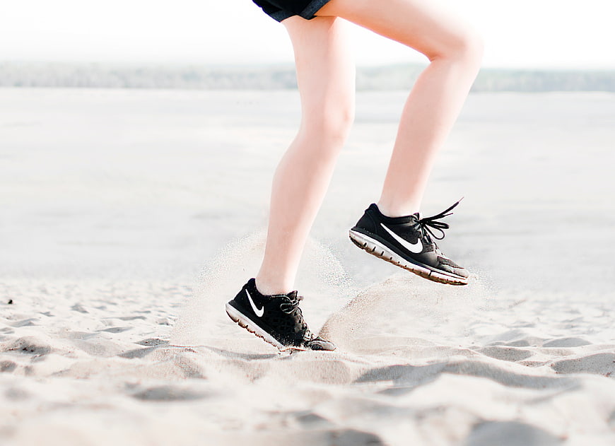 Woman Jumping in Sneakers on Sandy Beach