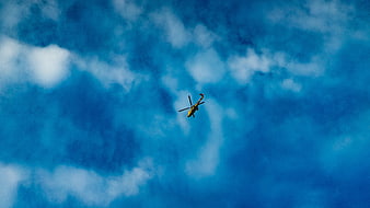 Yellow helicopter flying in blue sky with clouds
