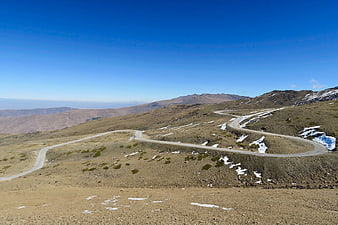 Winding mountain road with snow patches under blue sky