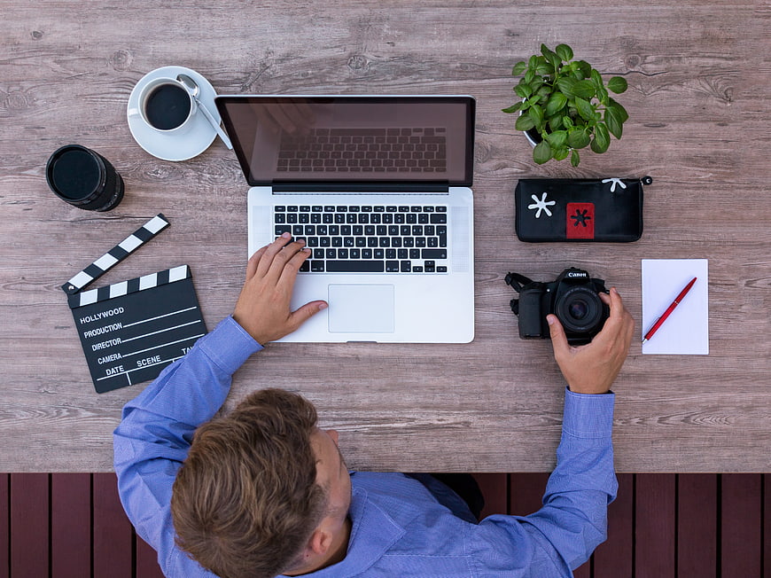 Top view of filmmaker working at desk with laptop and camera