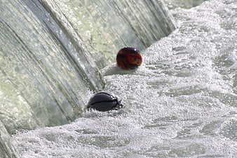 Two colorful balls floating in rushing water near a dam spillway