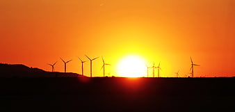 Wind Turbines Silhouette Against Vibrant Orange Sunset Sky
