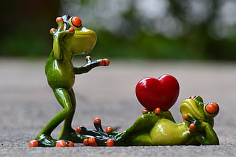 Cute ceramic frog figurines with red heart on stone surface