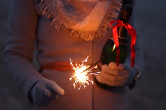 Woman holding sparkler and champagne bottle at night