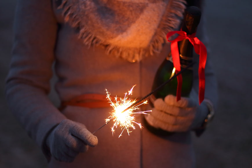 Woman holding sparkler and champagne bottle at night