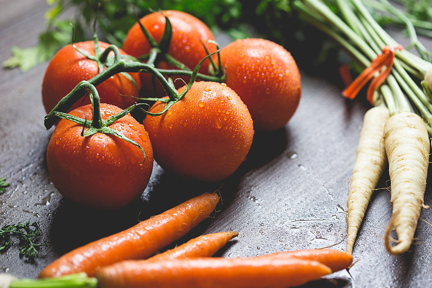 Fresh wet tomatoes, carrots, and parsnips on dark slate