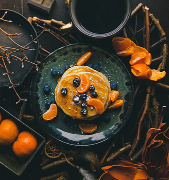 Overhead shot of pancakes with blueberries and mandarin oranges on dark plate