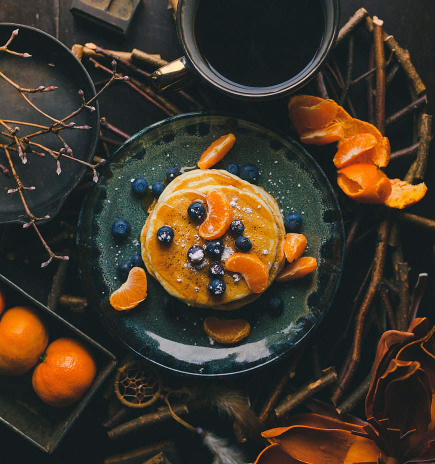 Overhead shot of pancakes with blueberries and mandarin oranges on dark plate