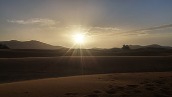 Sunset over sand dunes with lens flare and footprints