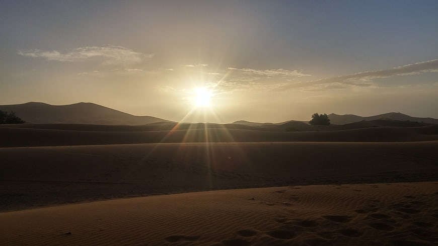 Sunset over sand dunes with lens flare and footprints