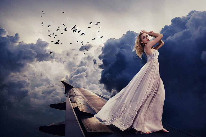 Woman in White Dress Standing on Airplane Wing in Clouds