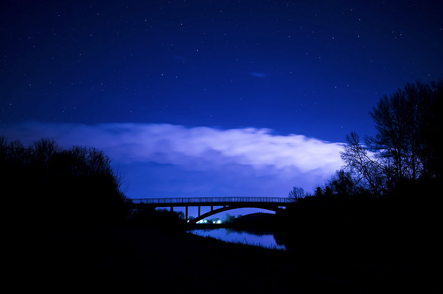 Silhouette of bridge over river under starry night sky