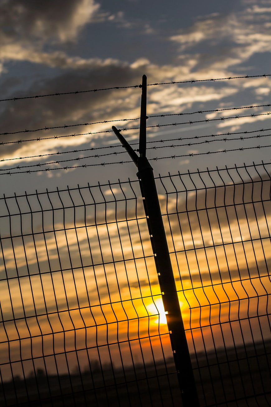 Silhouette of Barbed Wire Fence Against Golden Sunset Sky