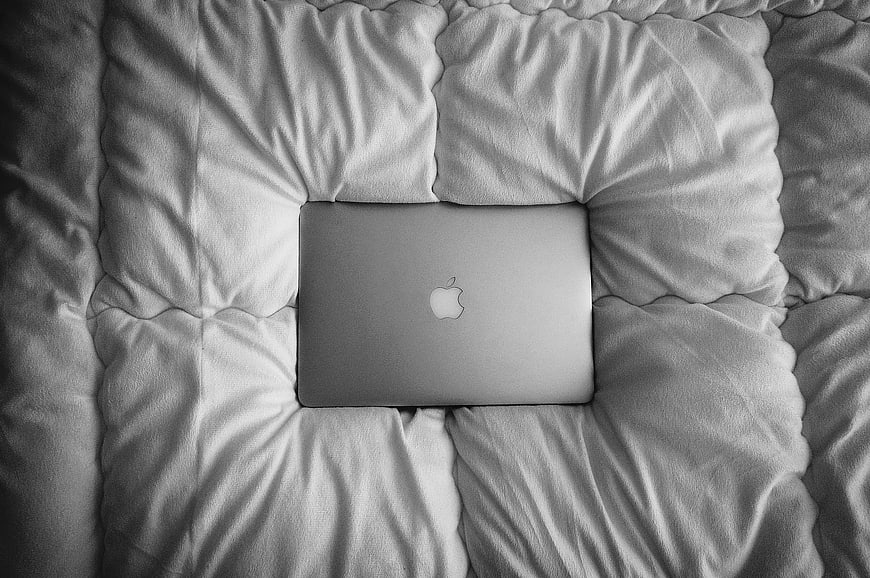 Closed silver laptop on white comforter top view