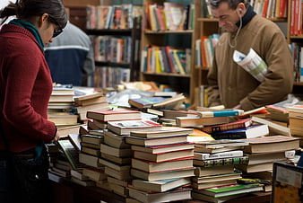 Woman and Man Browsing Piles of Books in Used Bookstore