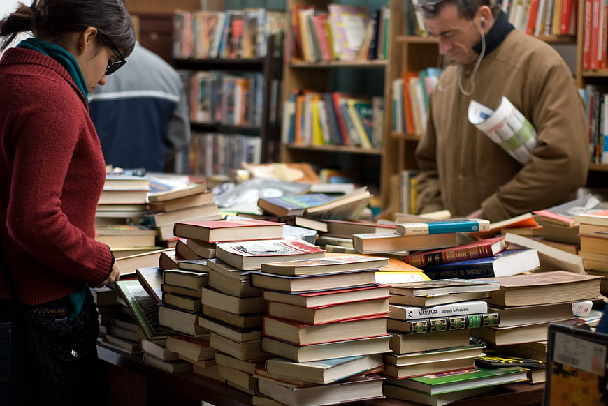Woman and Man Browsing Piles of Books in Used Bookstore