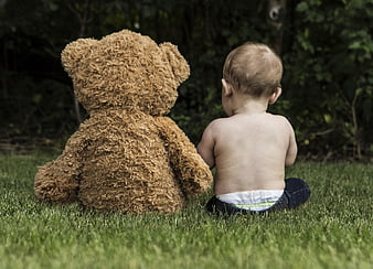 Baby sitting on grass with large teddy bear outdoors