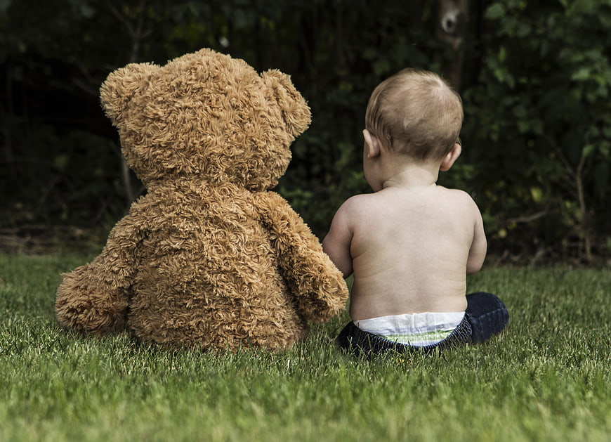 Baby sitting on grass with large teddy bear outdoors