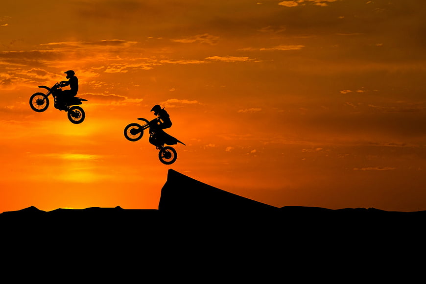 Two Dirt Bike Riders Silhouetted Against Vibrant Orange Sunset Sky