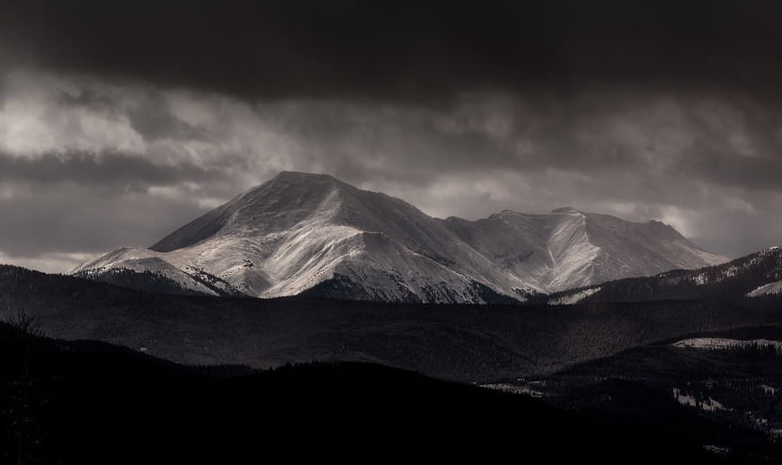 Dramatic Snow-Capped Mountain Peak Under Dark Stormy Clouds