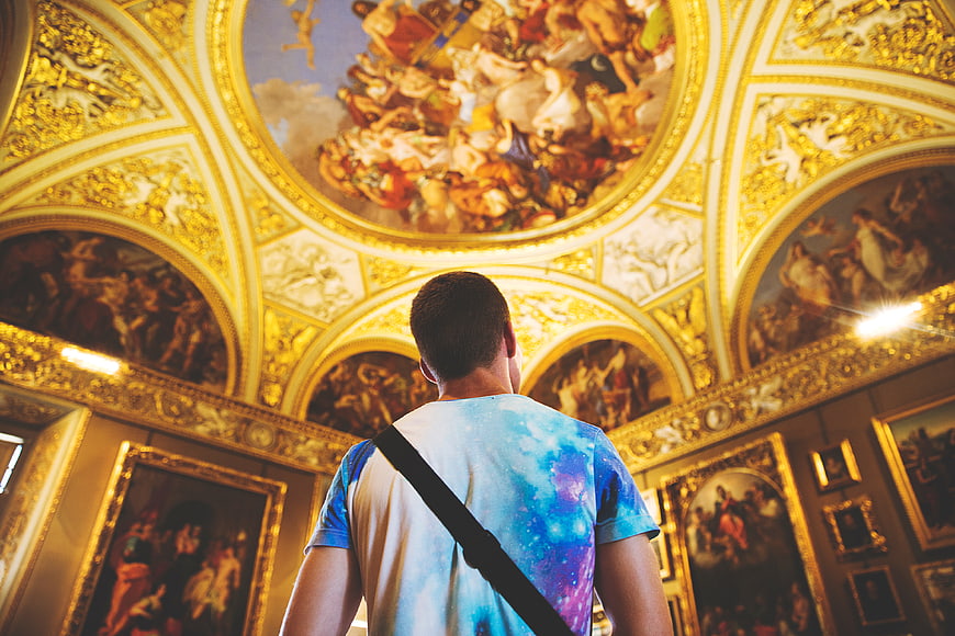 Man admiring ornate ceiling frescoes in a grand art museum