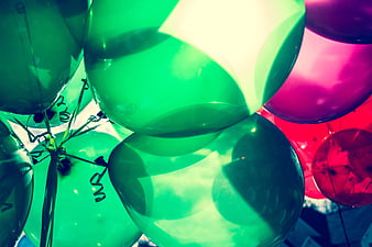 Colorful green and pink balloons against a bright sky