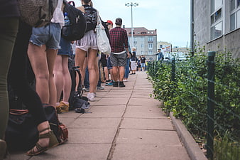 Low angle view of people standing in a long queue on a city sidewalk