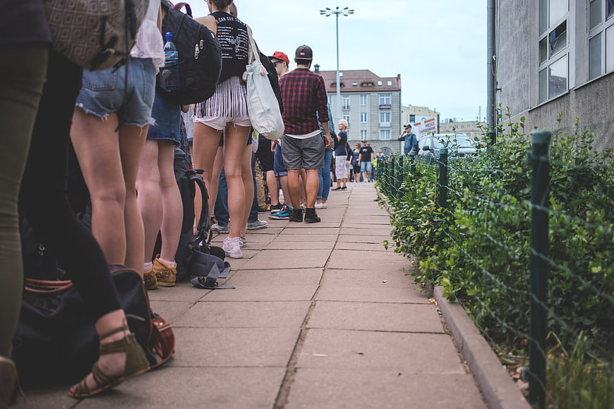 Low angle view of people standing in a long queue on a city sidewalk