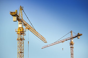 Two yellow construction cranes against a clear blue sky