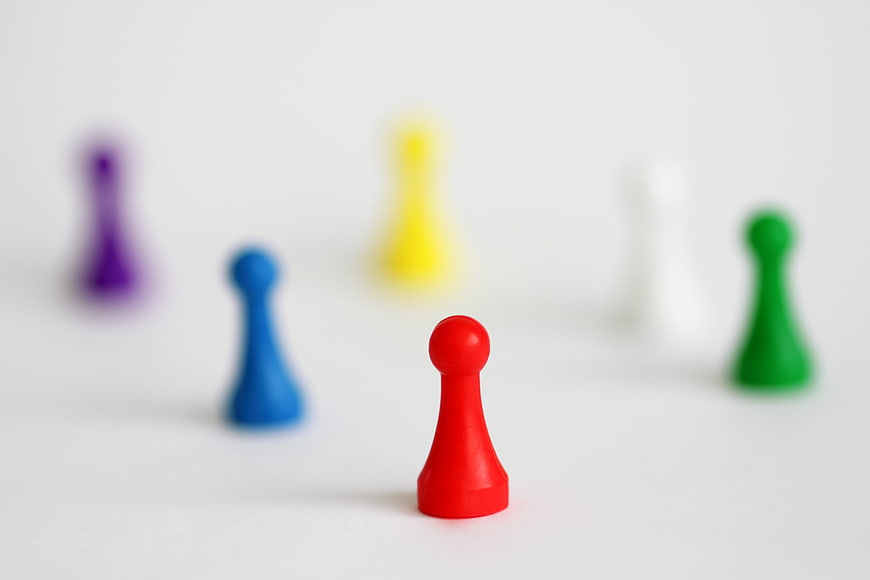 Red game pawn leading colorful team on white background