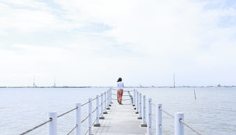 Woman standing on pier looking out at calm sea