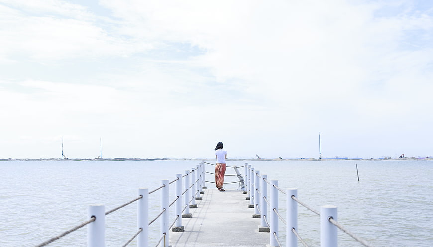 Woman standing on pier looking out at calm sea