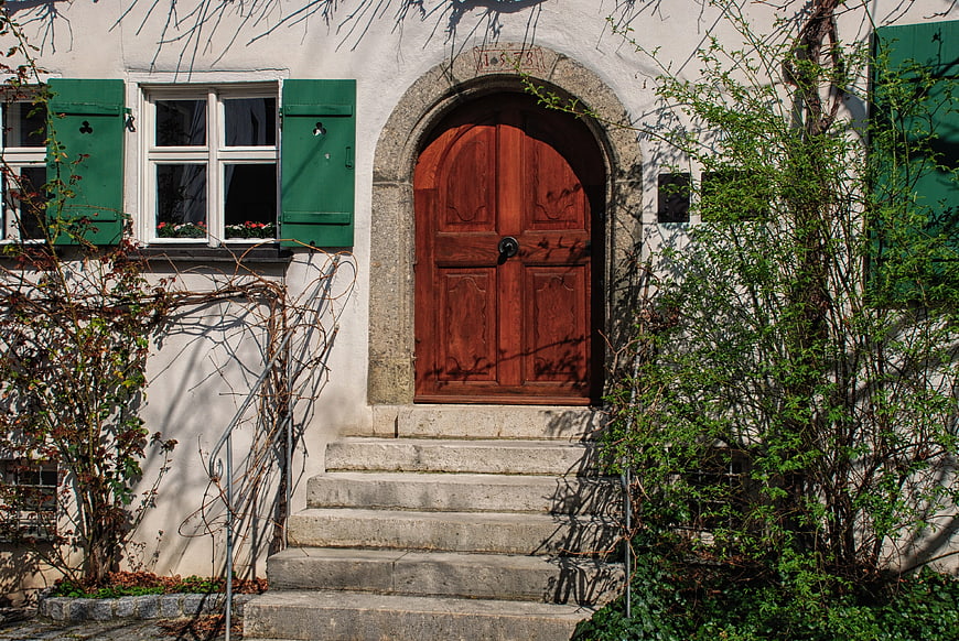 Rustic wooden arched door with green shutters and stone steps