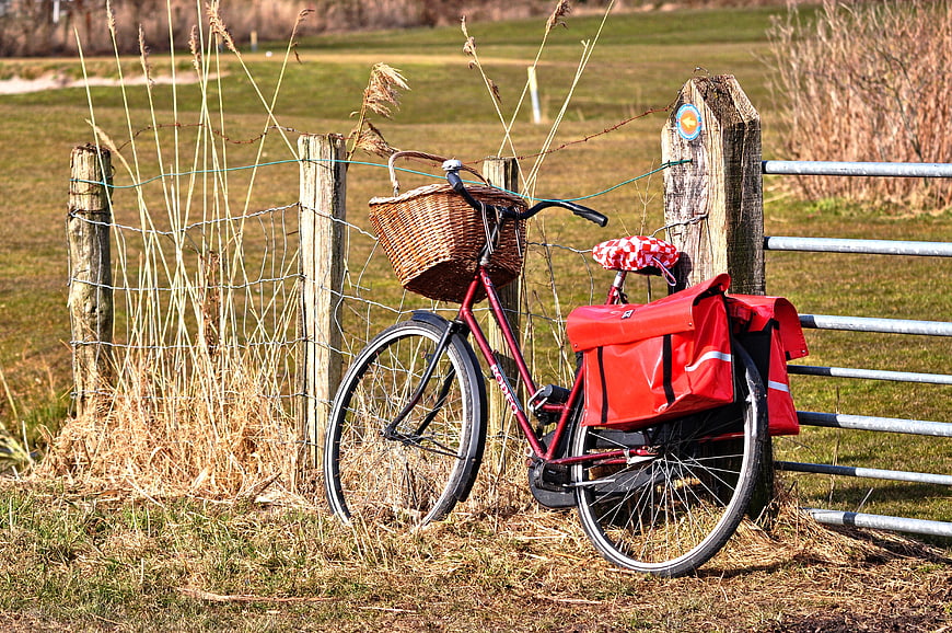 Red bicycle with wicker basket and panniers leaning on rural wooden fence