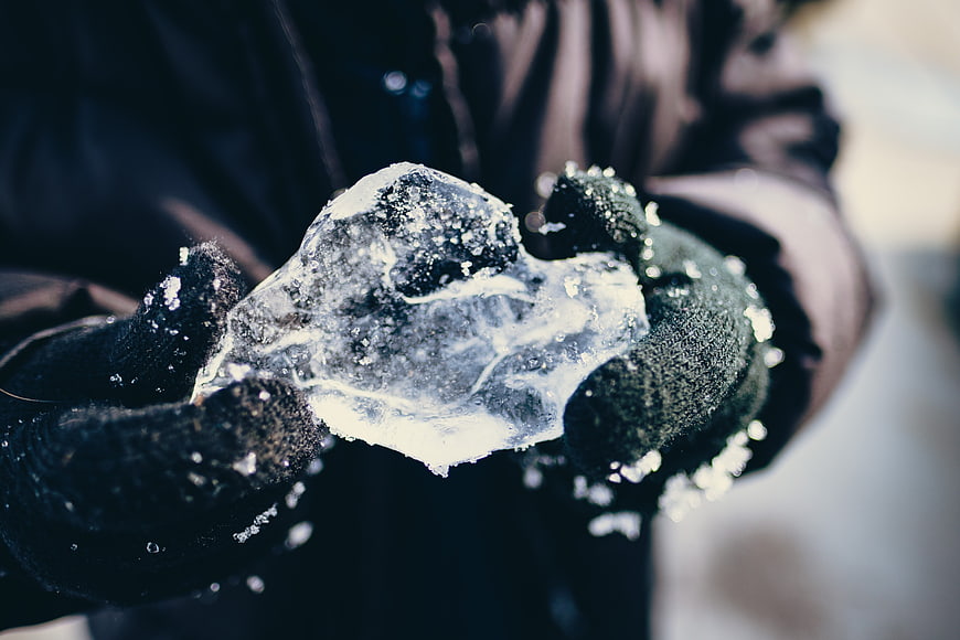 Gloved Hands Holding Chunk of Clear Ice in Winter