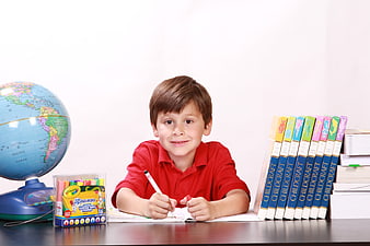 Smiling Boy Writing at Desk with Globe and Books
