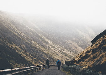 Two Hikers Walking on Mountain Road in Foggy Highland