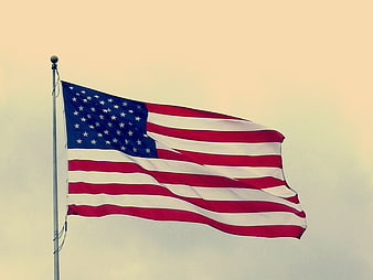 American flag waving against a soft, warm sky background