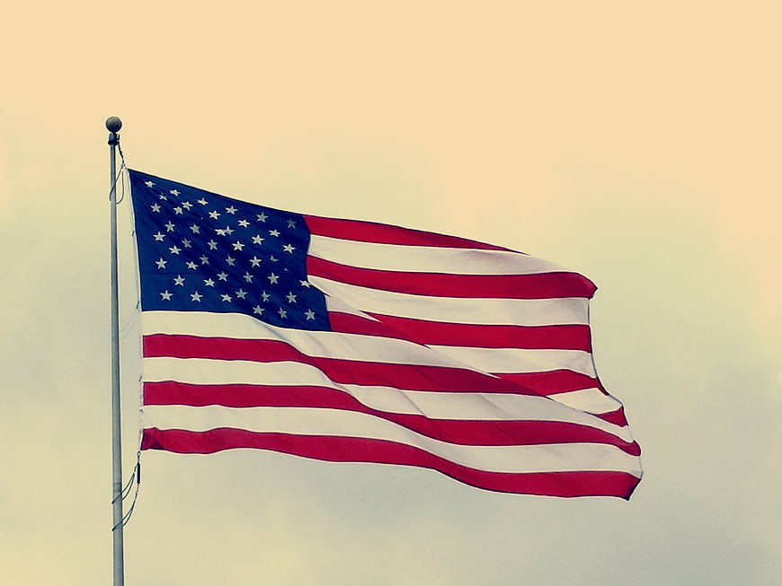 American flag waving against a soft, warm sky background