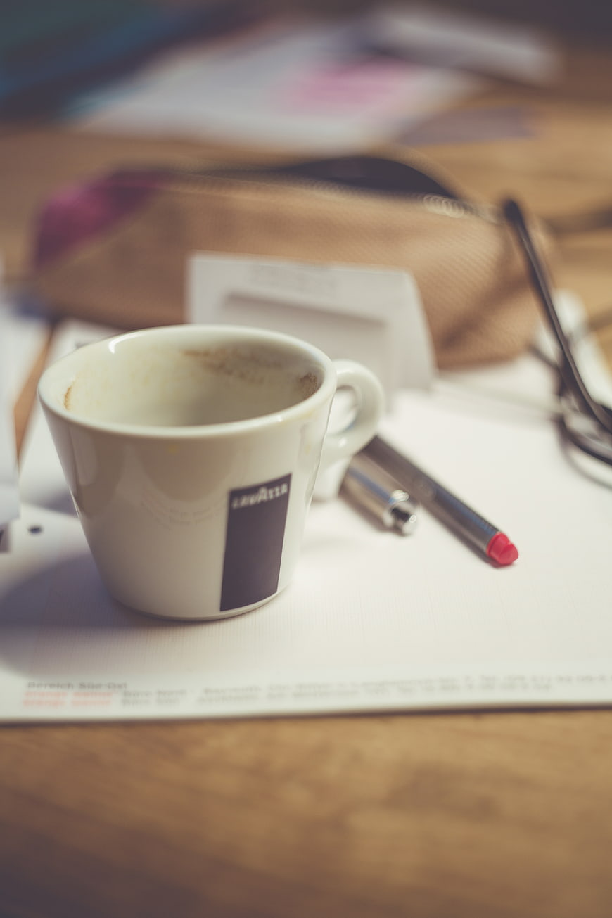 Empty coffee cup on cluttered office desk with pen and papers