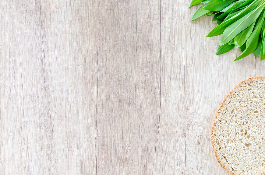 Fresh bread slice and green leaves on light wood background