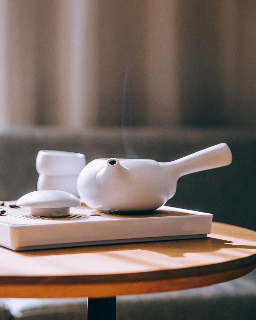 Steaming white ceramic teapot on wooden tray