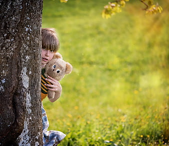 Child Hiding Behind Tree with Teddy Bear in Nature