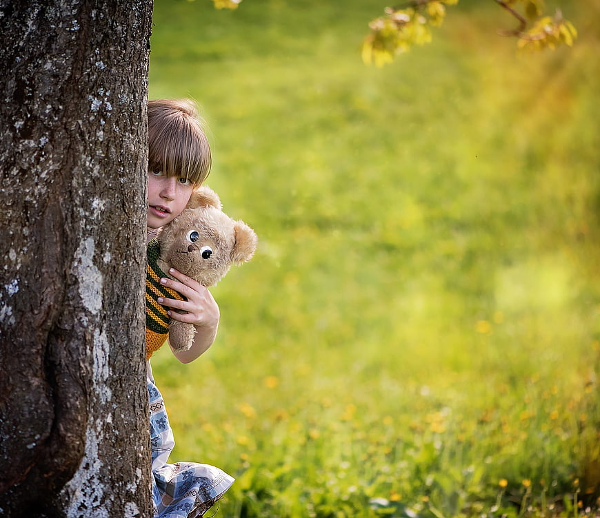 Child Hiding Behind Tree with Teddy Bear in Nature