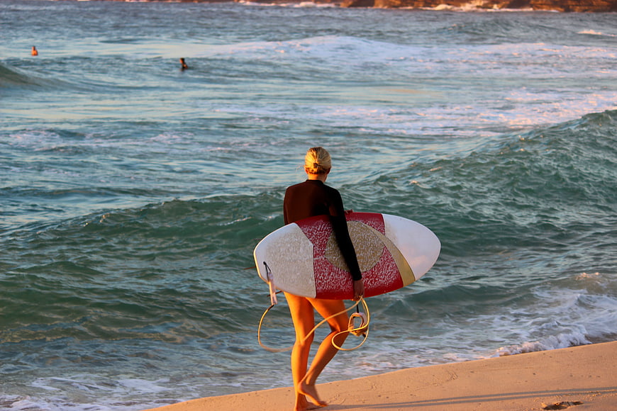 Female Surfer Walking on Beach with Surfboard at Sunset