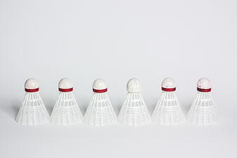 Row of six white badminton shuttlecocks on a light gray background