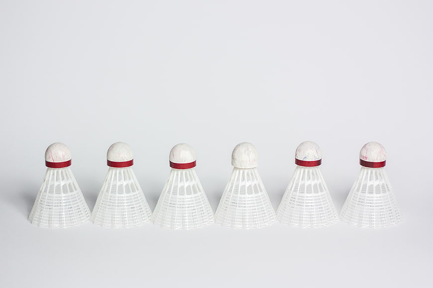 Row of six white badminton shuttlecocks on a light gray background