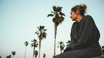 Woman in grey knit cardigan sitting with palm trees background