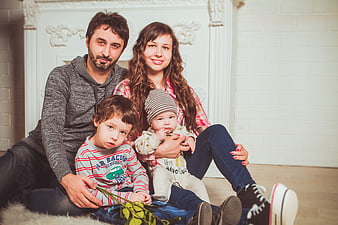 Family of four sitting on floor in front of white fireplace