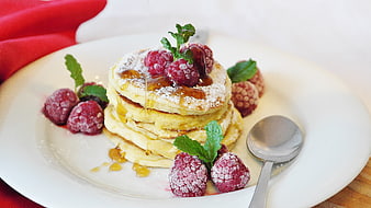 Stack of fluffy pancakes with raspberries and honey